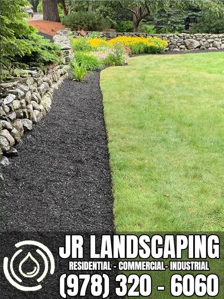 Black mulch bed along a fieldstone retaining wall with perennials
