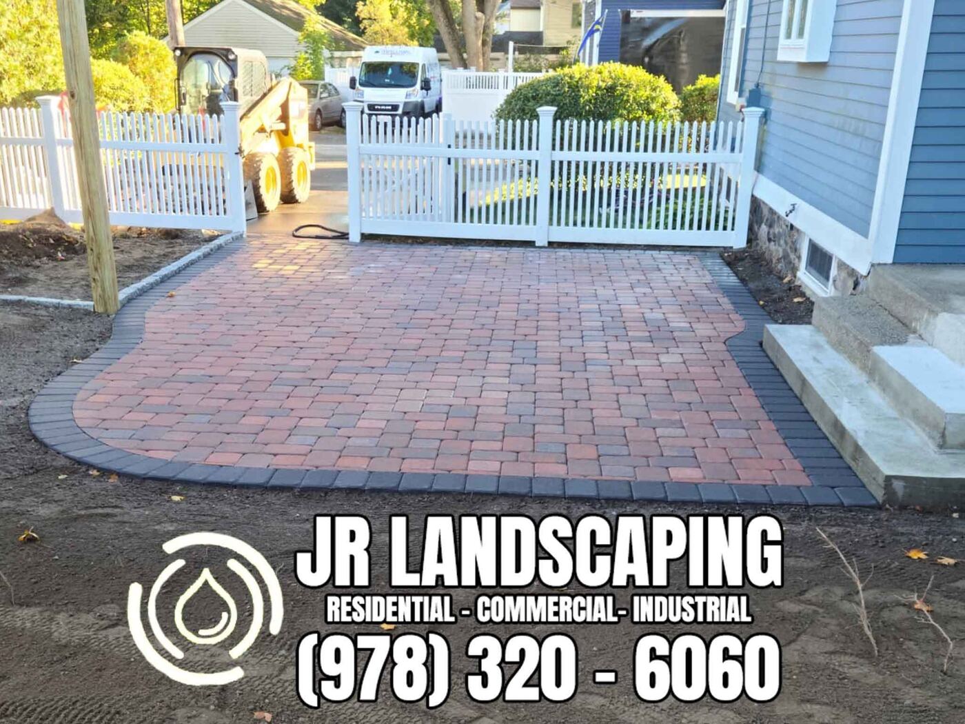 Red-and-charcoal paver patio bordered by a white vinyl picket fence